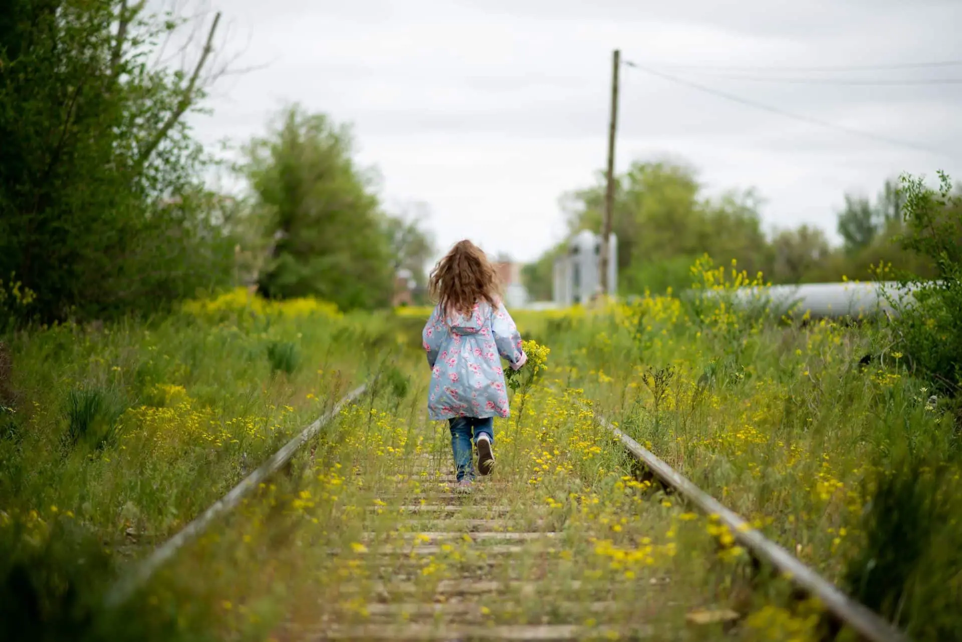 A little girl walks along the grassy railroad tracks.
