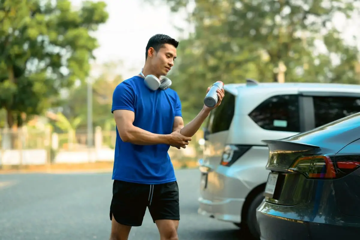 Male athlete in fitness clothes standing near his car while going to the gym.